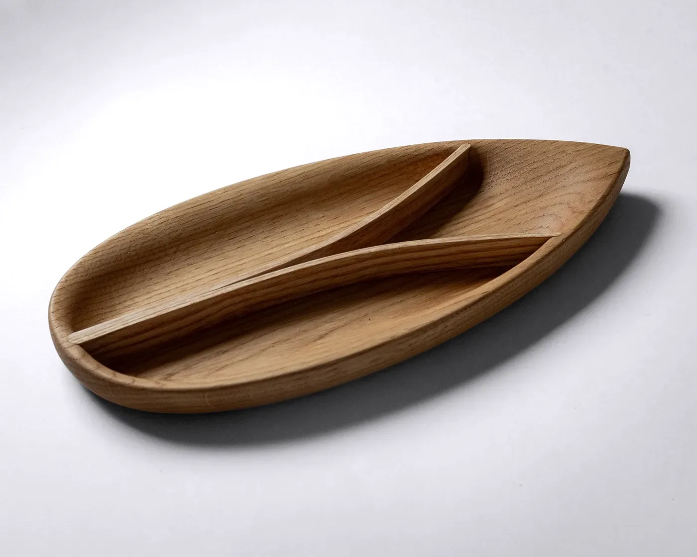 Bent wood tray in oak with ash dividers on a clean white surface, showing the leaf-shaped form