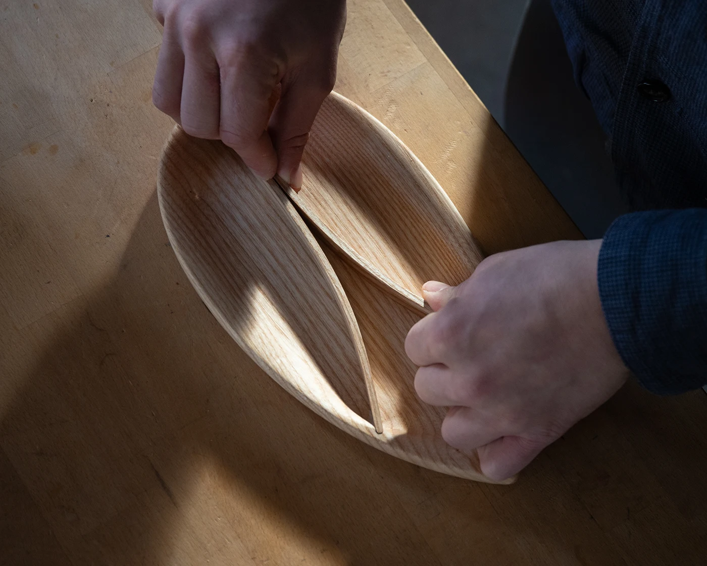 Hands shaping a steam-bent ash tray in the workshop, showing the pale grain and curved form