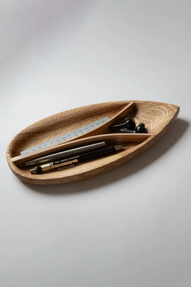Hands shaping a steam-bent ash tray in the workshop, showing the pale grain and curved form