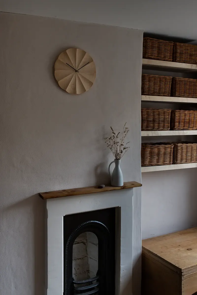 British sycamore wall clock with radial fluted face hanging above a fireplace in a contemporary interior