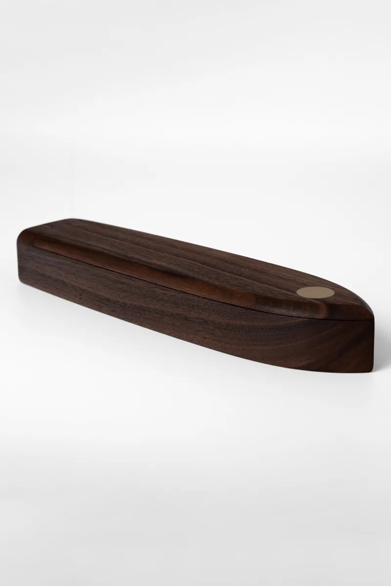 Low-angle view of the walnut pen box showing the curved hull profile and brass inlay